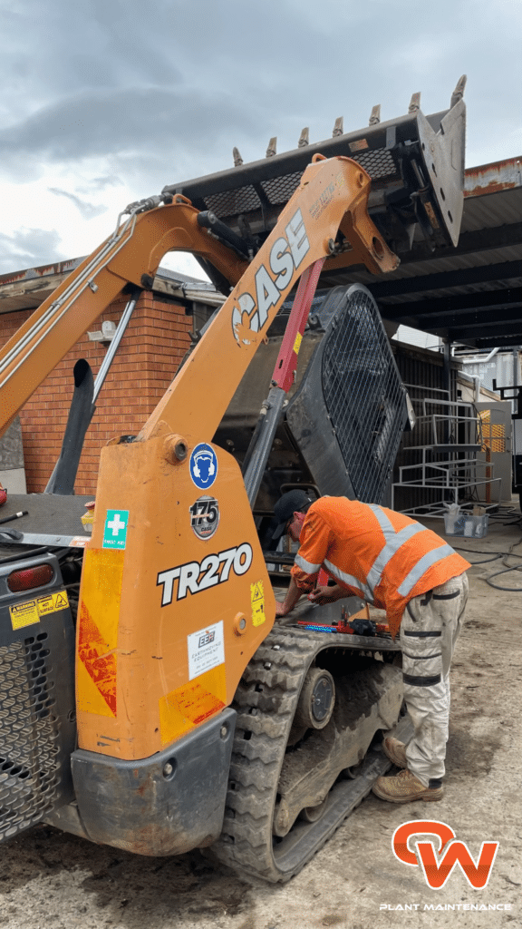 A worker in an orange vest repairs or inspects a CASE TR270 skid steer loader at a construction site.